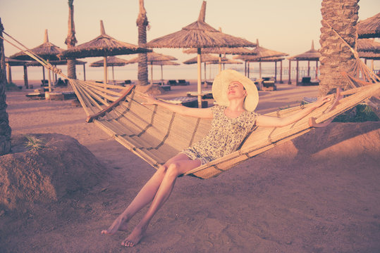 young woman in hat and yellow dress on hammock at sunset coast - Powered by Adobe