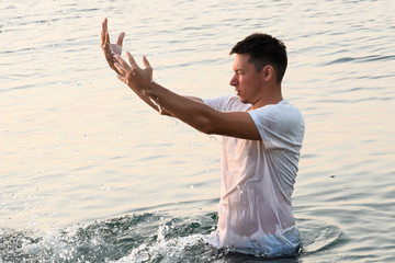 A handsome man stands in the water and creates a spray, a lot of