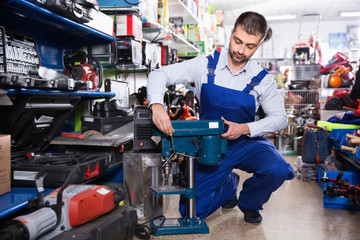 Adult male is standing with drilling machine in tools store.