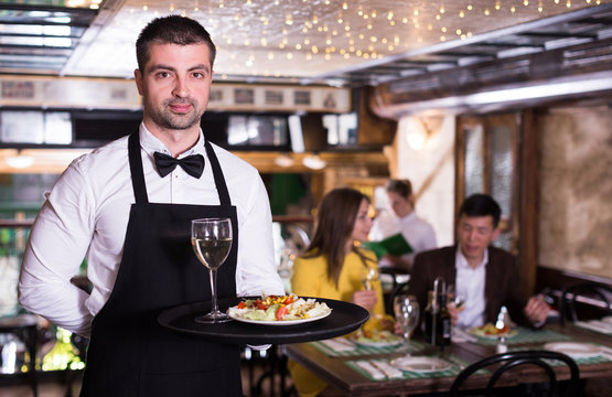 Portrait of male waiter who is holding tray with order