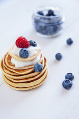 Delicious homemade pancakes with yogurt and fresh blueberries and raspberries on white wooden background.