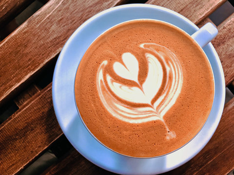Cup of cappucino on wooden table, mobile photo of hot drick with milk foam in heart shape latte art background