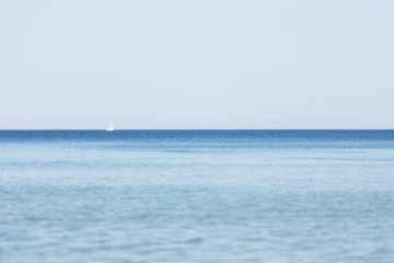 Obraz premium A white sailboat on the horizon of a body of water with blue skies