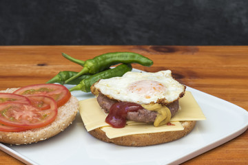 Hamburguesa con queso y huevo, acompañada de rodajas de tomate y pimientos picantes, preparada en casa 