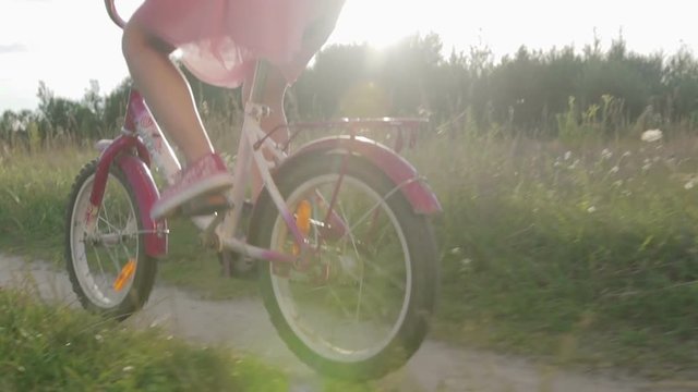 Girl in pink skirt rides a children's bike on the track, bike close-up