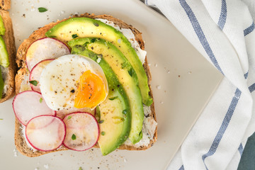 Sandwiches with avocado radish cheese and eggs on a rye bread on wooden board on dark background. Healthy breakfast. Vegetarian food.