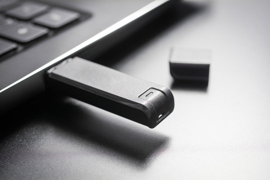 Macro Of A Black USB Memory Stick Plugged Into The USB Port Of A Black Laptop, Side View
