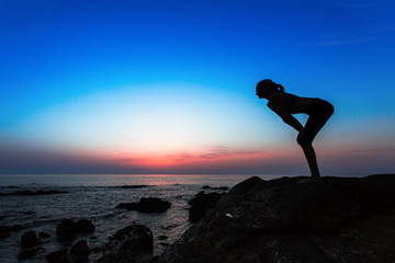 Silhouette of young woman doing gymnastics exercises on the Sea during sunset.