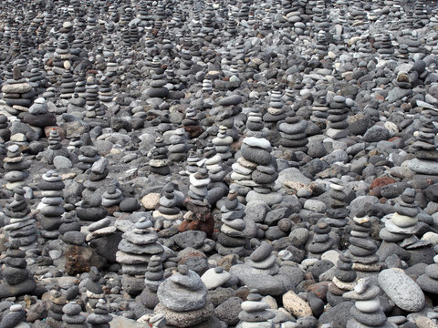 grey pebbles and stones on a beach arranged into a large collection of piles and towers filling the frame
