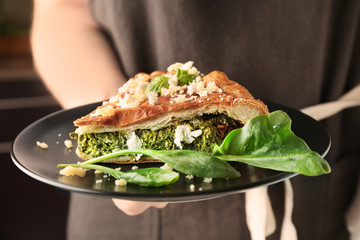 Woman holding piece of tasty pie with spinach on plate, closeup