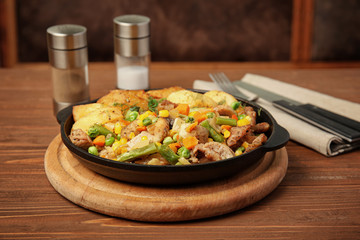 Pan with fried potatoes, meat and vegetables on wooden table