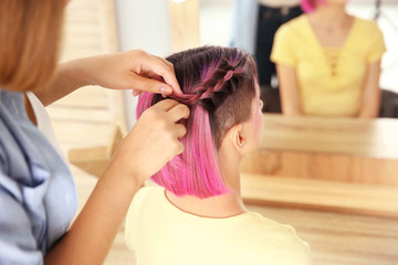 Professional stylist braiding woman's color hair in beauty salon. Modern trend