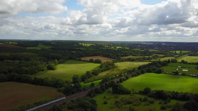 Drone aerial view over rural country side of UK with train going past. Day time wide shot.