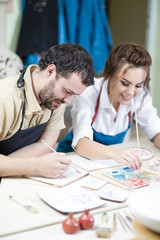 Naklejka premium Pottering Ideas. Caucasian Ceramists Painting and Glazing Clay Crafts Together in Workshop Using Paintbrushes. Woman Looking at camera.