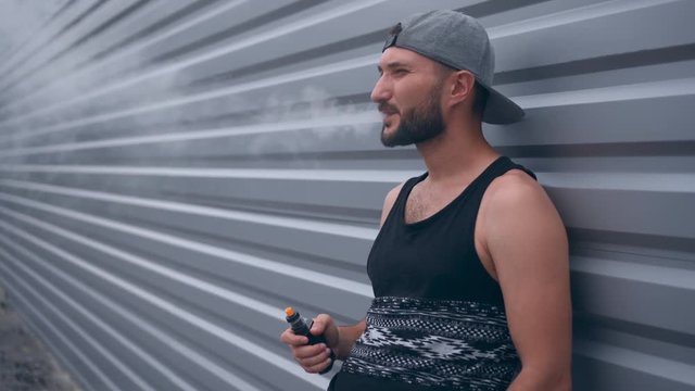 Modern man with beard smoking electronic sigarette outdoors