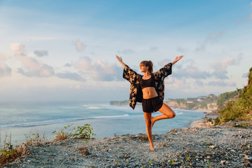 Woman practices yoga and meditates on the cliff in Bali.