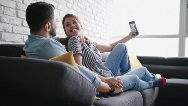 Young Couple Taking Selfie On Sofa At Home