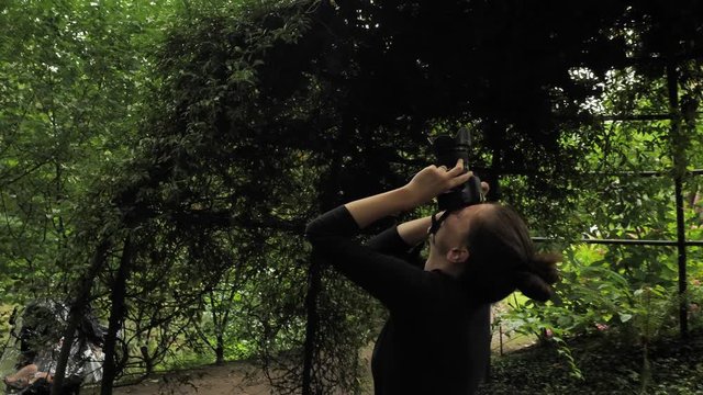 4k beautiful girl in black handmade dress standing inside of oval summer garden metal arbor construction shooting photo with dsl premium objetive in slow motion round moving motion camera