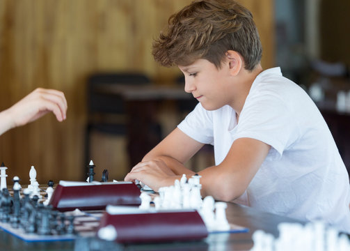 cute handsome boy in white tshirt plays chess with his rival in chess class. Education concept, intellectual game. Chess tournament, lesson, camp, training concept 