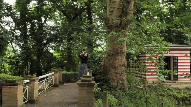 4k beautiful girl in black handmade dress standing inside of oval summer garden metal arbor construction shooting photo with dsl premium objetive in slow motion round moving motion camera