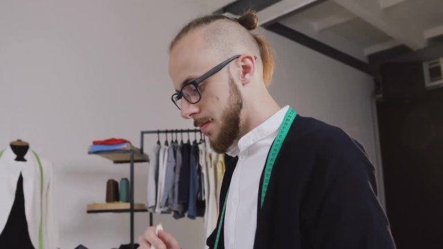 Designer sits on the table and draw sketches in the Studio. Designer drawing sketches for clothes. Handsome bearded designer working in atelier, sketching a fashion project