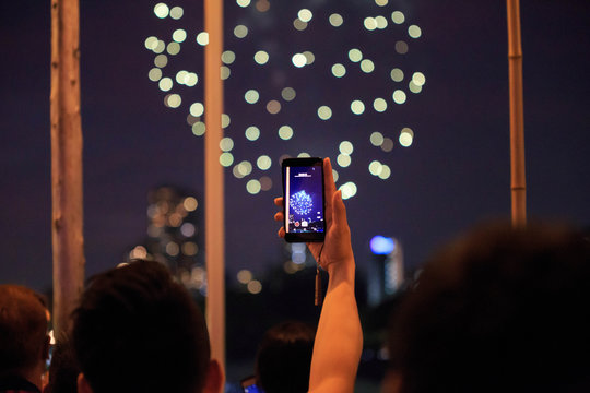 Man holding cellphone with one hand to record beautiful fireworks display