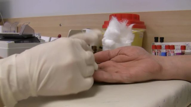 Close up of female nurse taking male patient's blood from finger in the medical laboratory. Blood tubes vials rotating in the background 