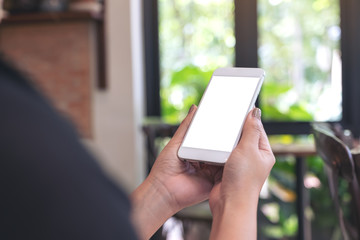 Mockup image of a woman holding and looking at a white smart phone with blank desktop screen with blur green nature background