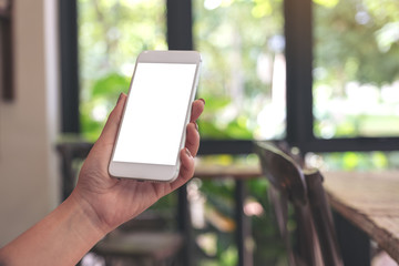 Mockup image of a woman holding and looking at a white smart phone with blank desktop screen with blur green nature background