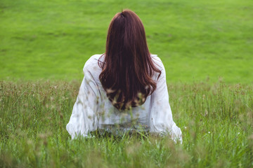 Back view of a woman sitting alone in the park with with beautiful grass flower  background