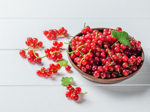 Freshly picked redcurrant berries in a clay bowl with leaves on a white wooden table.