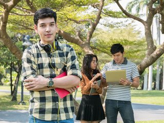 Handsome young college student holding books and smiling while his friends standing on background