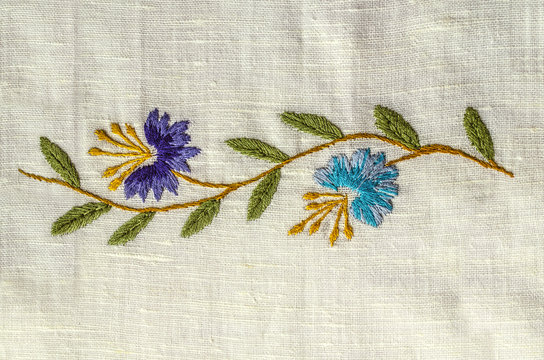 Embroidered satin stitch wavy sprig with
 purple and blue cornflowers with leaves on the rough cotton fabric


