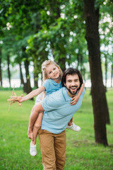 Fototapeta premium adorable daughter piggybacking on happy father and playing with toy plane at park