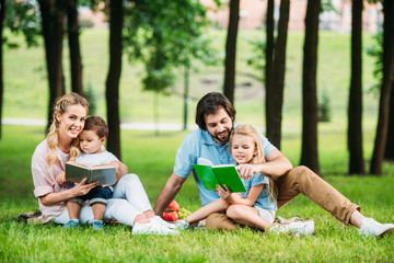 beautiful young family sitting on grass at park and reading books
