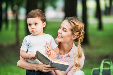 happy mother with sad little son reading book at park