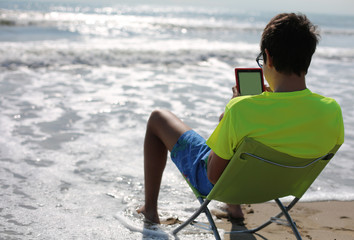 Fototapeta premium young teenager reads a digital book in front of the sea