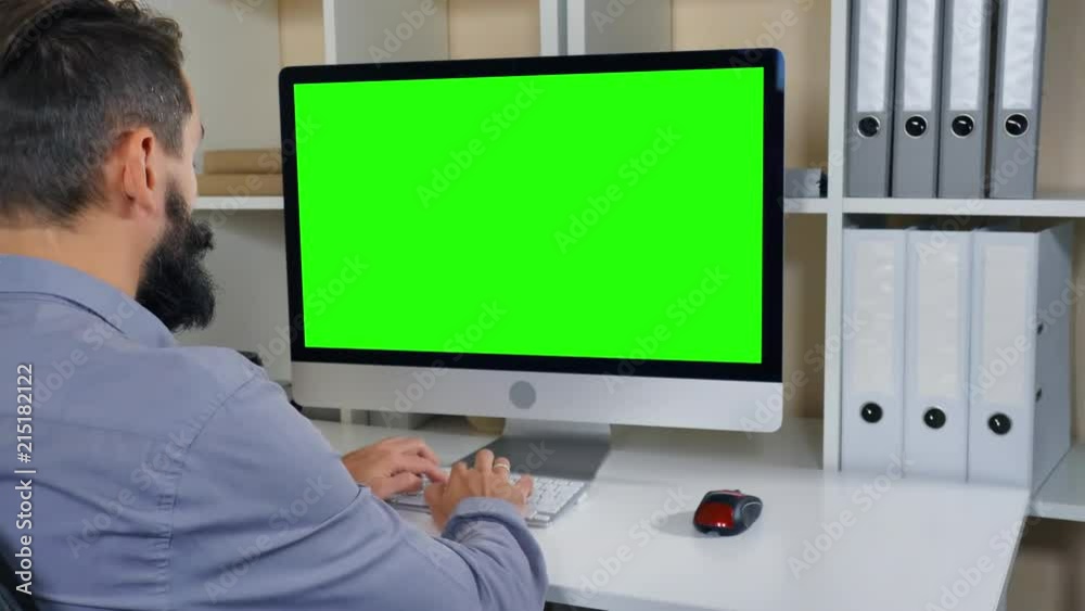 Aufkleber businessman sitting at workplace in small office. man with beard looking on display computer with green screen. employee in startup company typing on keyboard
