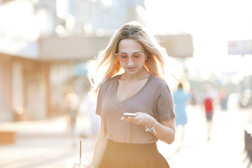 Outdoor fashion hipster style portrait of beautiful blonde woman drinking cocktail on the street