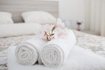White and fresh laundered fluffy towels with flower on bed in hotel