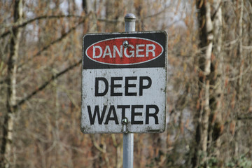 A danger deep water sign on a metal post in the woods.