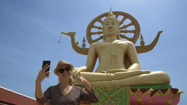 Young Caucasian Female Tourist Taking Selfie with Big Buddha Statue - Symbol and Main Landmark of Samui Island in Thailand. Tourism and Sightseeing