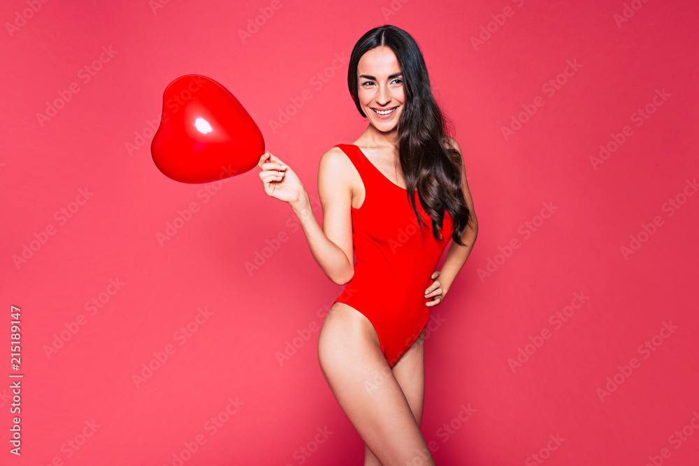 Wall mural happy beautiful young smiling woman with long curly hair in red swimsuit posing over pink background