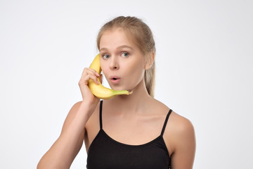 Pretty caucasian blonde woman holding banana like phone. Concept of communication