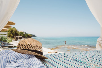 Obraz premium Straw hat lying on the beach bed with beauty view to blue the ionian sea, clear sky and girl in water on Greek island Zakynthos in landscape orientation