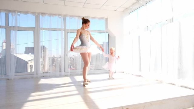Happy mother in ballet outfit playing with her little daughter and smiling cheerfully.
