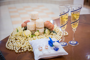 Two wedding glasses with champagne, and pair of gold rings on pillow, on table