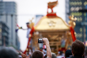 Western man holds arm high above crowd to take picture of omikoshi at Japanese summer festival