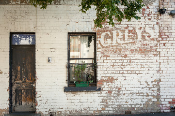 the remains of and old painted sign on the side of a building with a brown wooden door and window with planter box