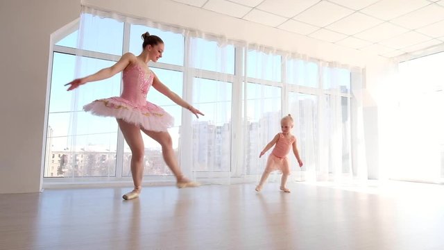 Young gorgeous ballerina with her little daughter dancing in studio. Happy ballerina with her child girl standing on tiptoes. Mother and daughter dancing ballet